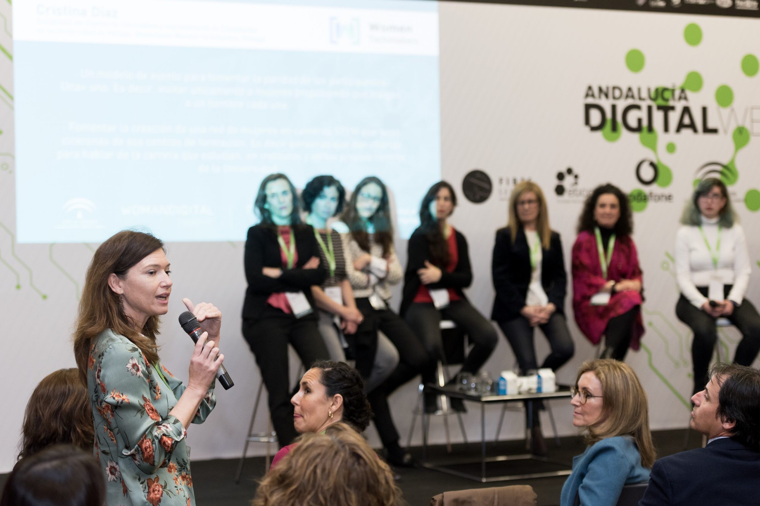 Grupo de mujeres desde el escenario escucha a un aparticipante del público hablando con un micrófono