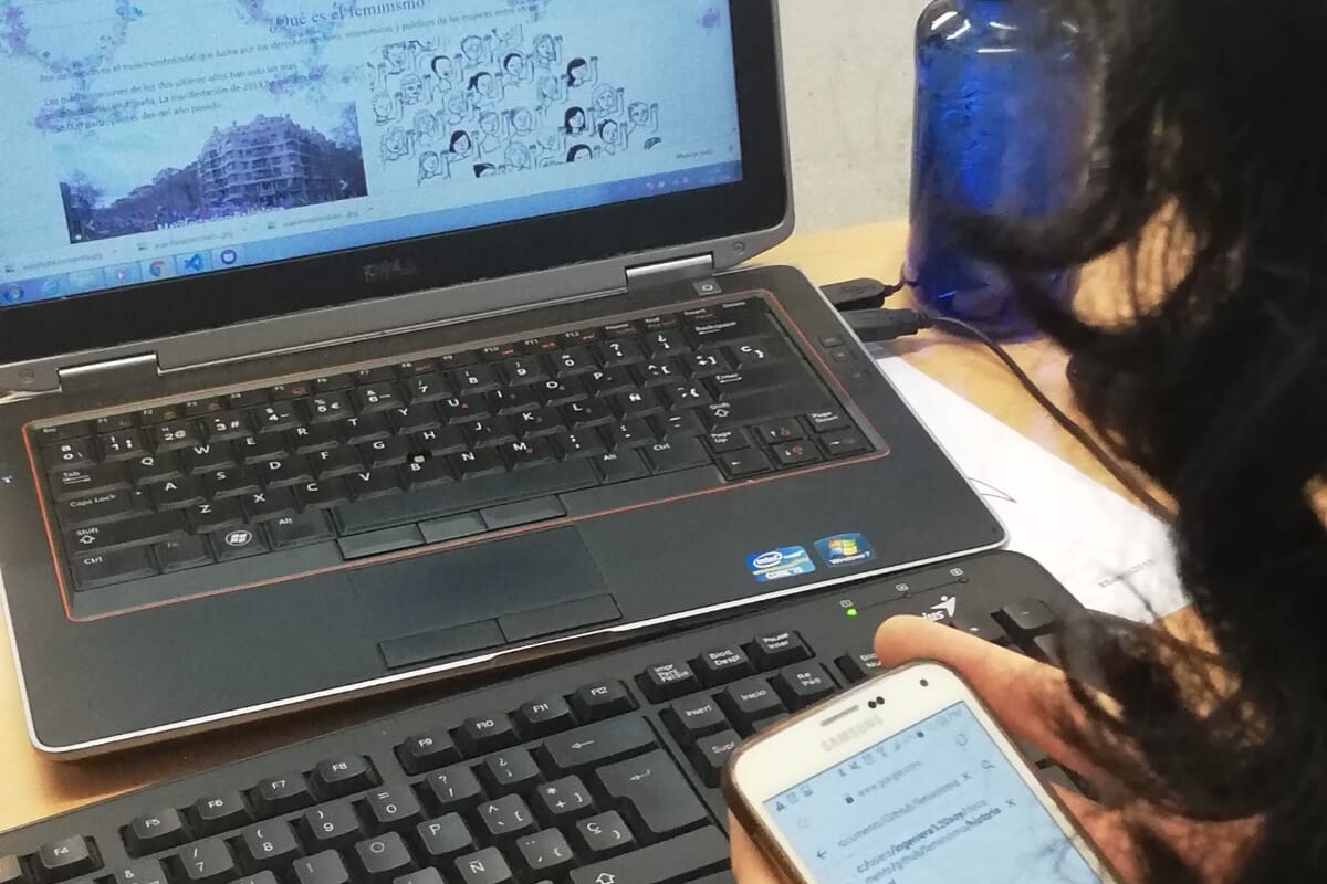 Una chica escribe en un teléfono móvil mientras trabaja con un ordenador portátil