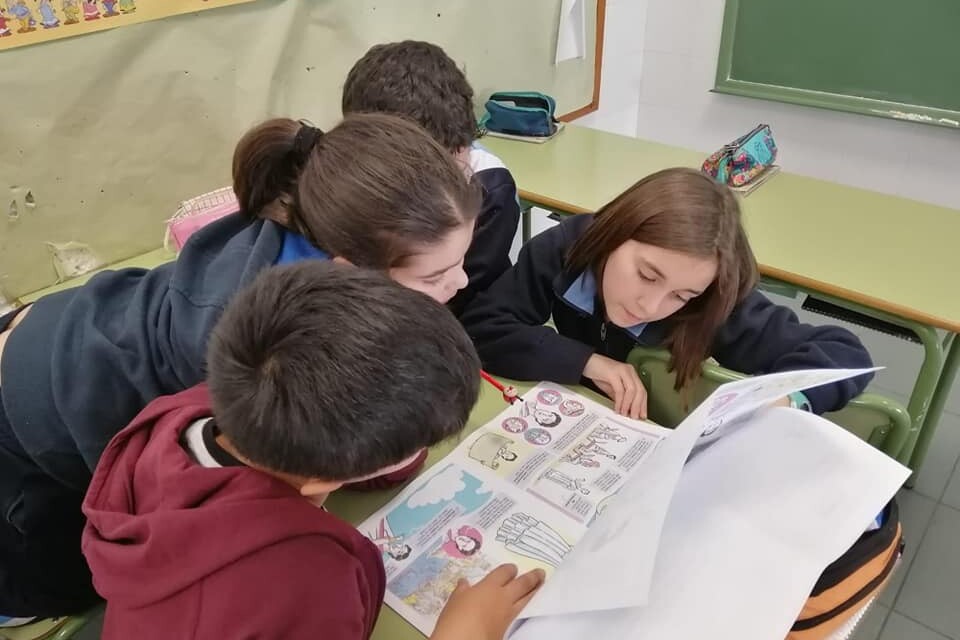En un aula, dos niñas y dos niños leen información sobre mujeres importantes en la historia de la ciencia y tecnología