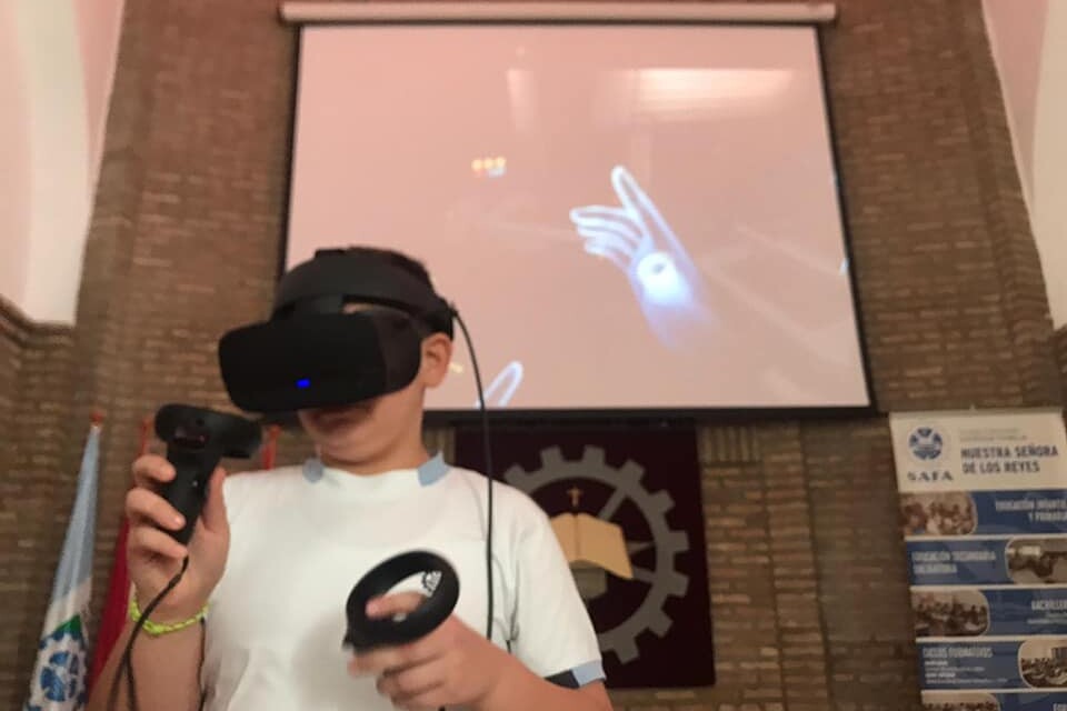 Un alumnos utiliza unas gafas de realidad virutal, hay una pantalla de proyector al fondo donde se proyecta lo que se visualiza con las gafas