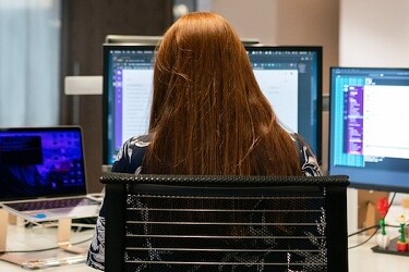 mujer de espaldas trabajando en varios ordenadores