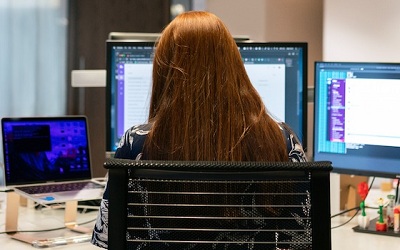 mujer de espaldas trabajando en varios ordenadores