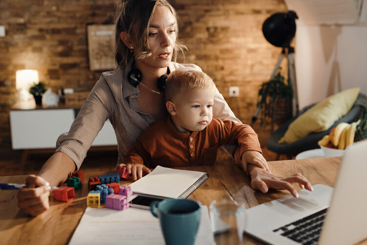 Una mujer trabaja con un portátil con su hijo en brazos
