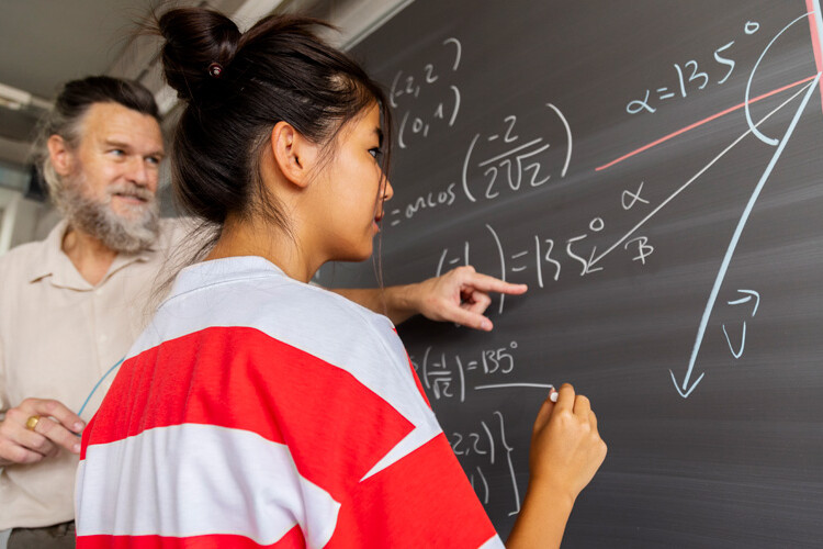 Una chica hace ecuaciones en una pizarra con el profesor
