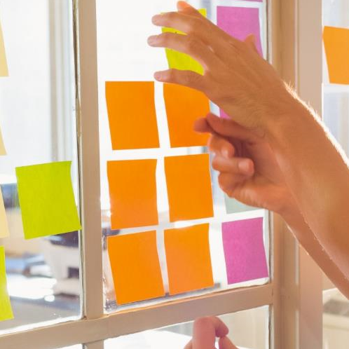 Personas utilizando post-it en una pared para organizar el trabajo